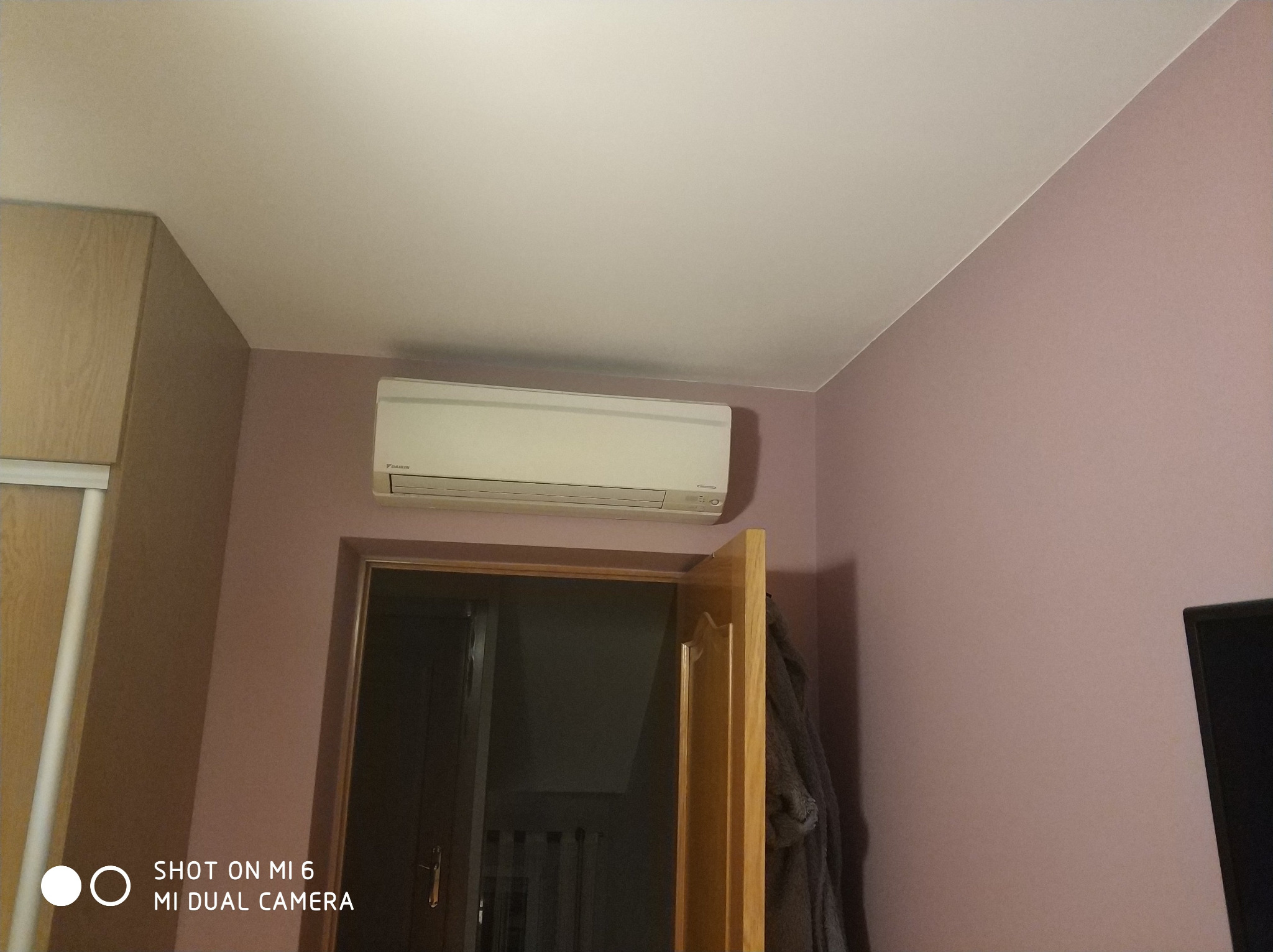 Zamontowany klimatyzator Daikin na fioletowej ścianie nad otwartymi drzwiami w pokoju, widoczny fragment szafy i telewizora.