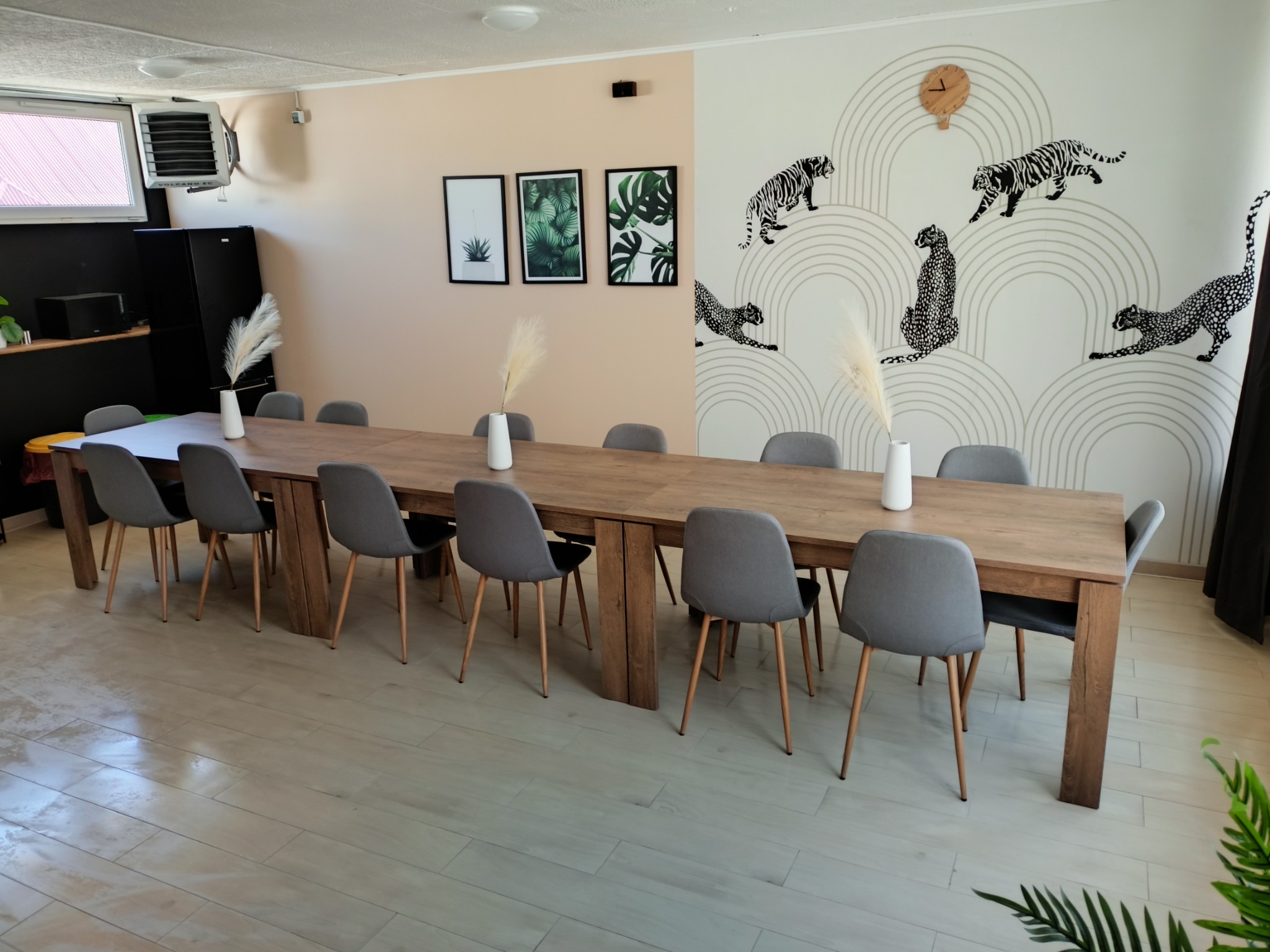 Sala konferencyjna z długim drewnianym stołem, szarymi krzesłami, dekoracjami ściennymi z motywem zwierzęcym i roślinnymi grafikami w ramkach.