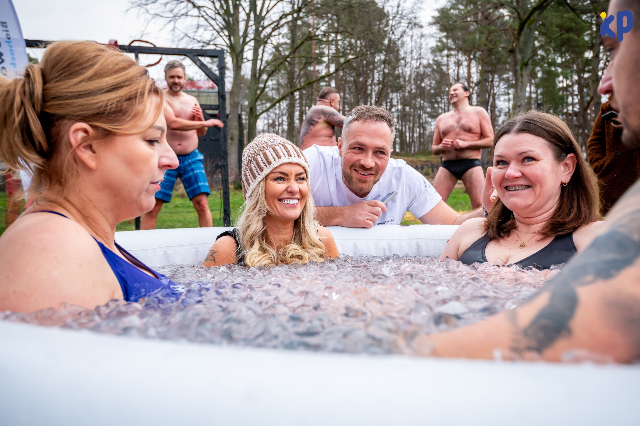 Morsowanie w Gdańsku: Grupa osób zanurzona w lodowatej wodzie w plenerze. Uśmiechnięte twarze, widoczny las w tle, biała wanna z lodem. Ekstremalna terapia.