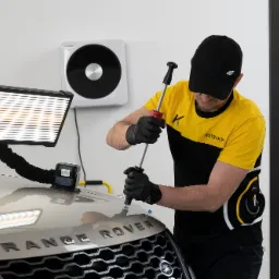 Technik PDR usuwa wgniecenie na masce Range Rovera przy użyciu specjalistycznego oświetlenia i narzędzi, widoczne przyssawki na masce.