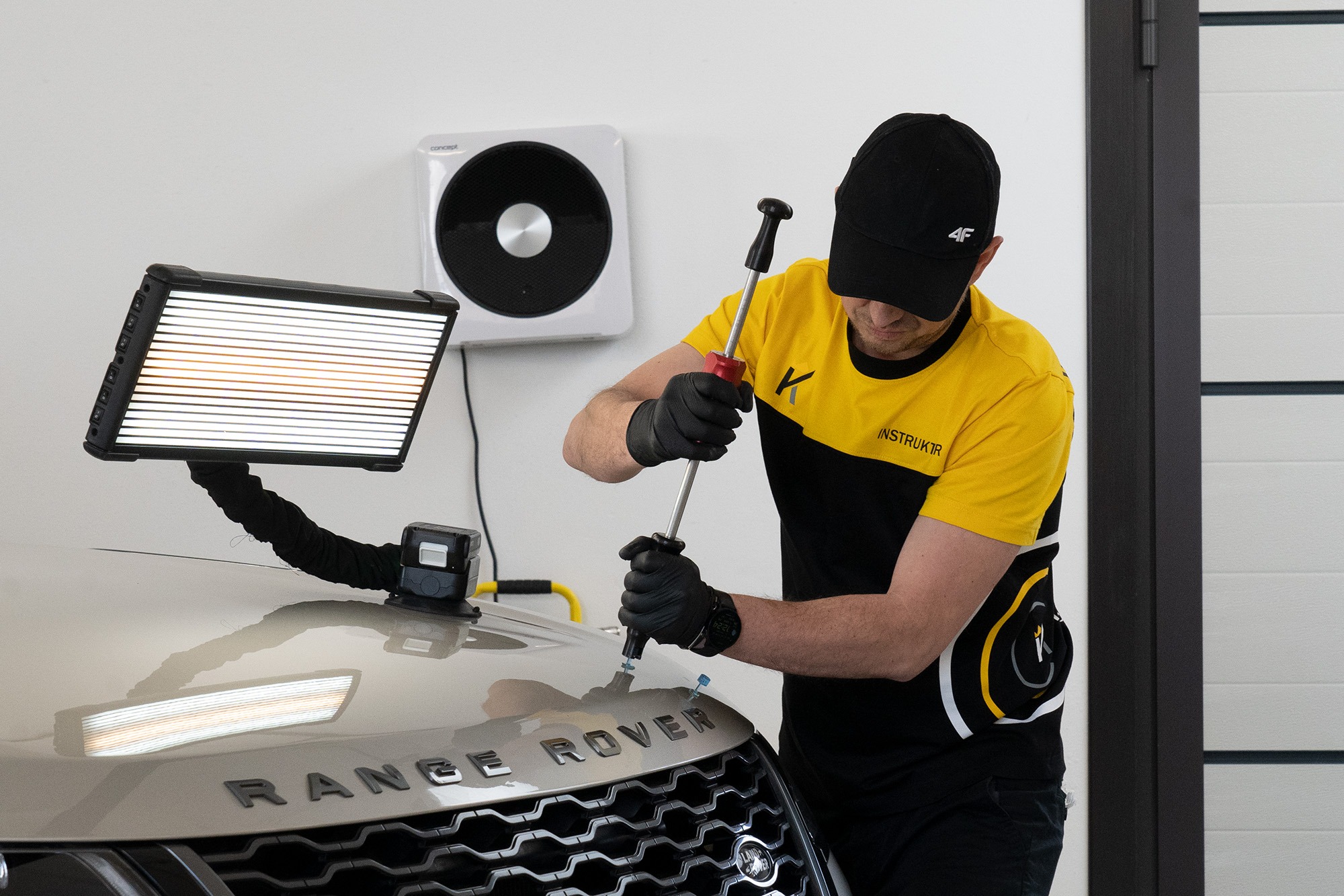 Technik PDR usuwa wgniecenie na masce Range Rovera przy użyciu specjalistycznego oświetlenia i narzędzi, widoczne przyssawki na masce.