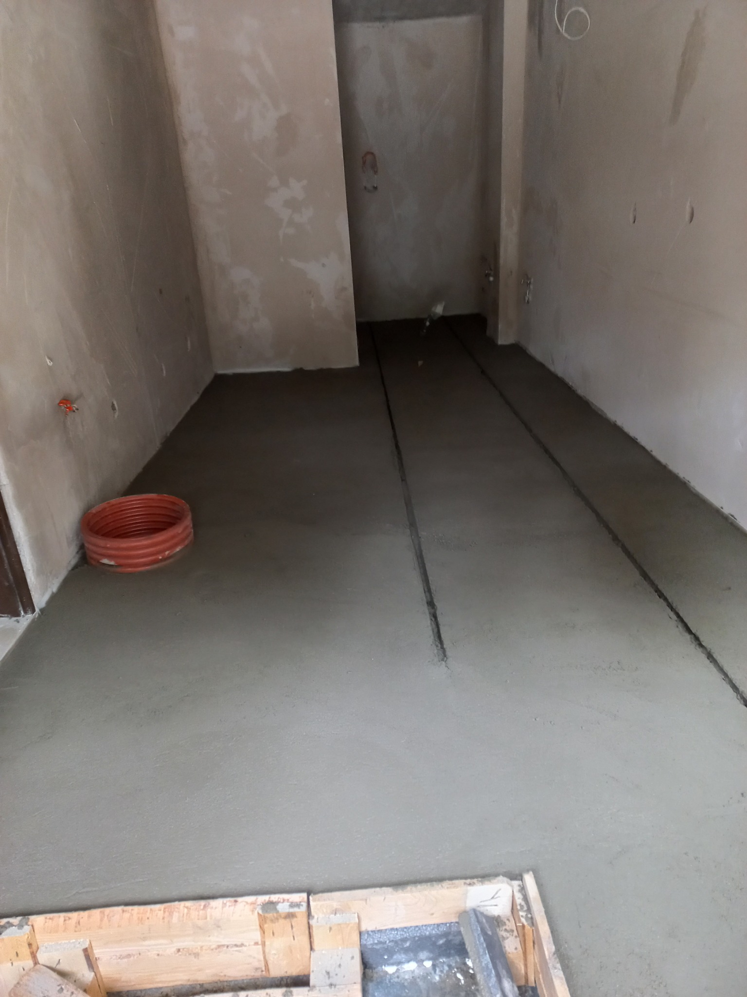 Wylewka betonowa na podłodze w trakcie realizacji, widoczne rury instalacyjne i drewniane szalunki.