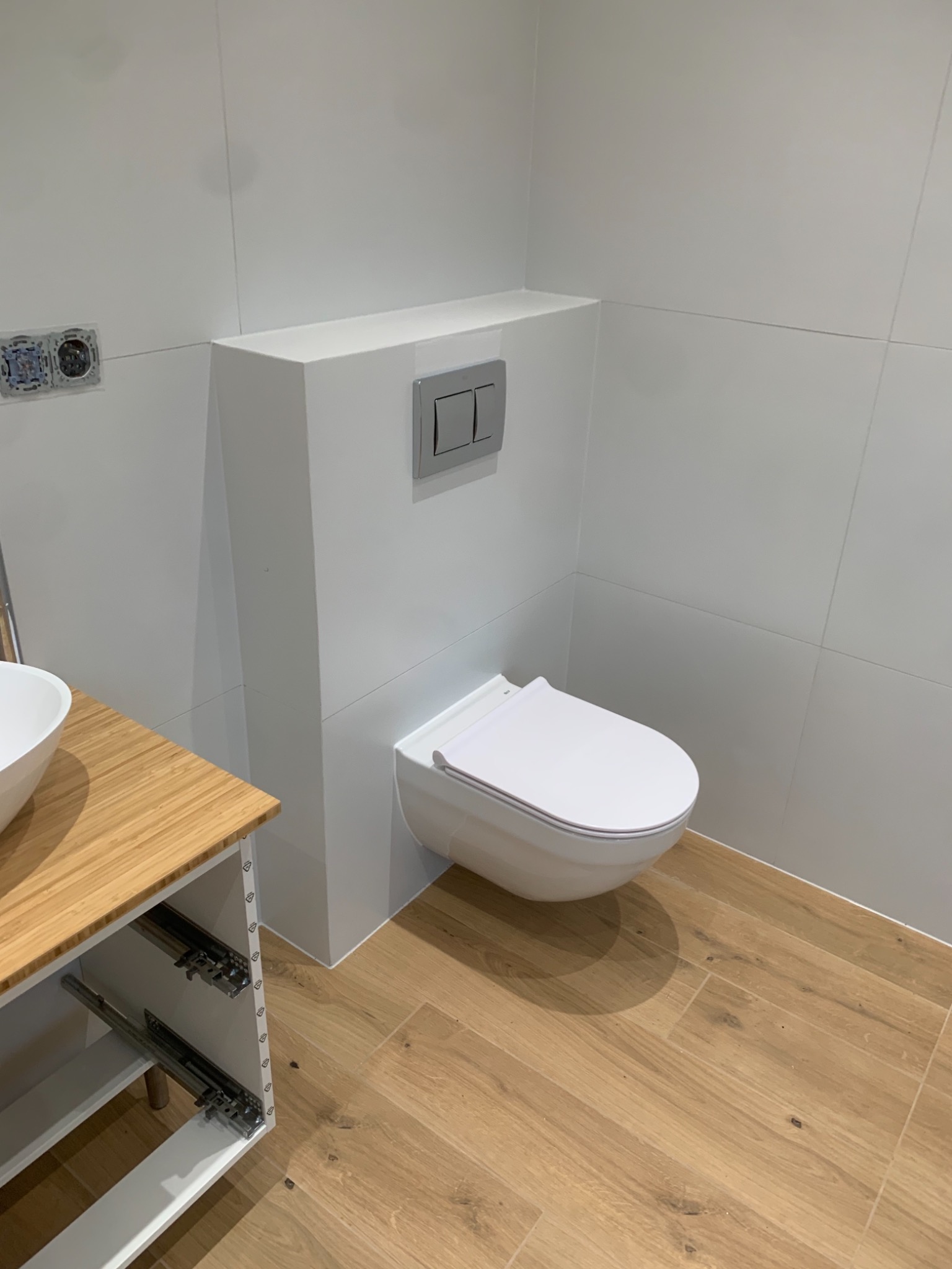 Nowoczesna łazienka z podwieszaną toaletą, drewnopodobną podłogą i umywalką na bambusowym blacie, widoczne puszki elektryczne przed wykończeniem