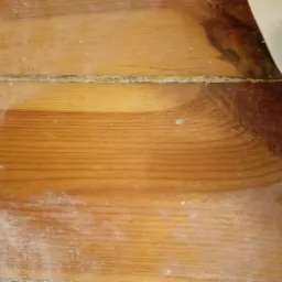 Fragment drewnianej podłogi po szlifowaniu, widoczne ślady pyłu i nierówności w szczelinach między deskami.