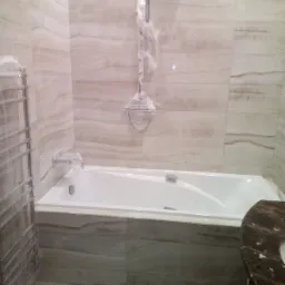 Nowa, jasna łazienka z wanną, marmurowym blatem umywalki i grzejnikiem drabinkowym, elementy armatury zabezpieczone folią ochronną.