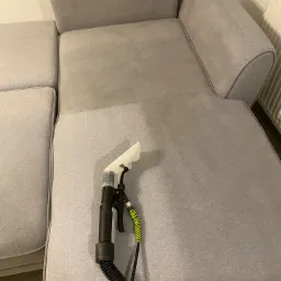 Czyszczenie jasnoszarej sofy za pomocą ekstraktora z przezroczystą dyszą; widoczna r&oacute;żnica w odcieniu po czyszczeniu.