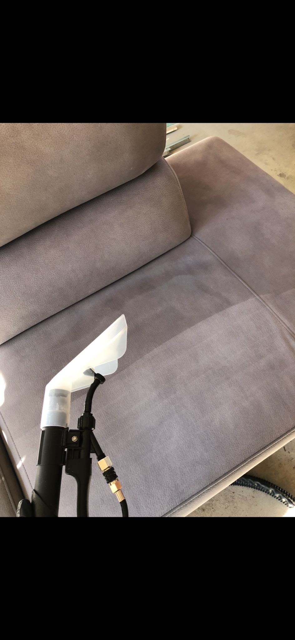 Dysza ekstraktora do czyszczenia tapicerki pozostawia wyraźny ślad czyszczenia na szarej, welurowej sofie.