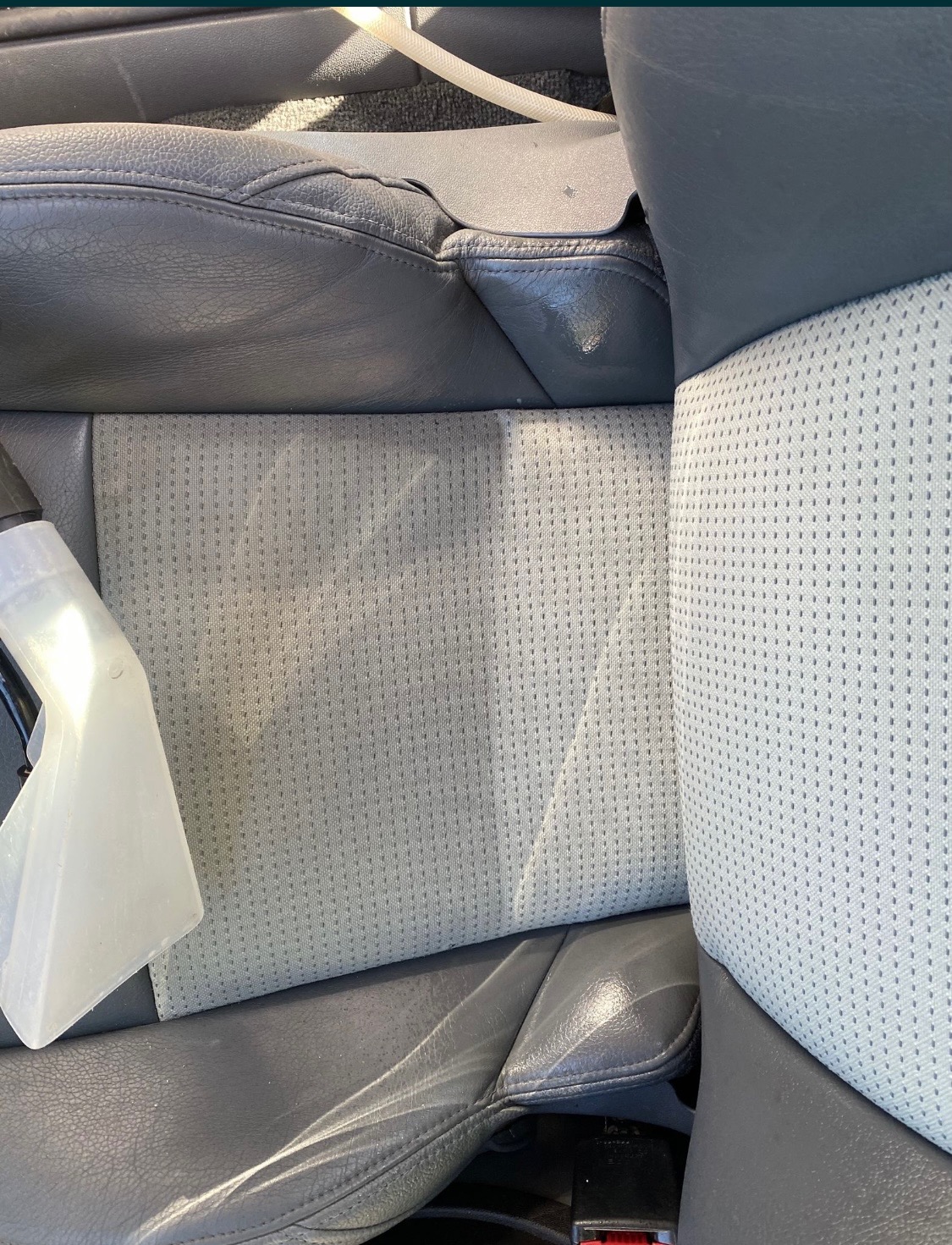 Czyszczenie tapicerki samochodowej jasnoszarą dyszą parową, widoczna różnica w kolorze między wyczyszczoną a brudną powierzchnią fotela.