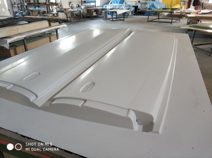 Dwie białe, identyczne formy z tworzywa sztucznego, prawdopodobnie do odlewania elementów, leżące na stole w warsztacie, widoczne ślady obróbki.