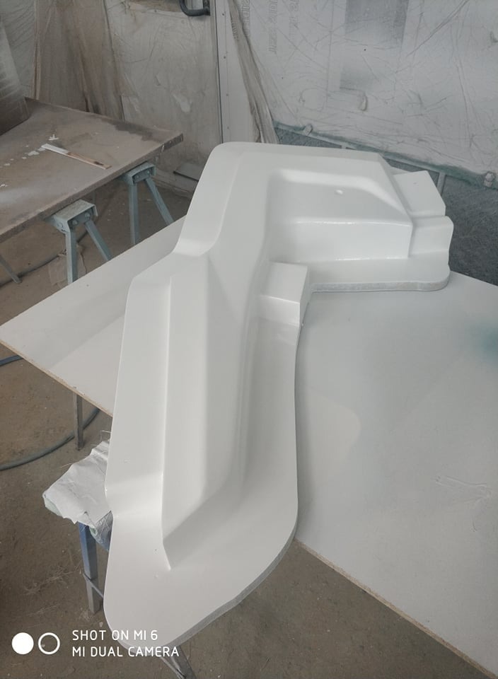 Biały, niestandardowy element z tworzywa sztucznego o złożonej geometrii, leżący na stole roboczym w warsztacie.