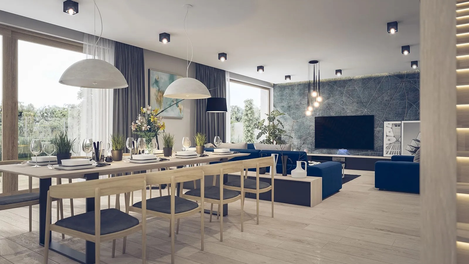 Przestronny salon z jadalnią w nowoczesnym stylu, z dużym stołem z krzesłami z jasnego drewna, niebieską sofą i ścianą z motywem liści za telewizorem.