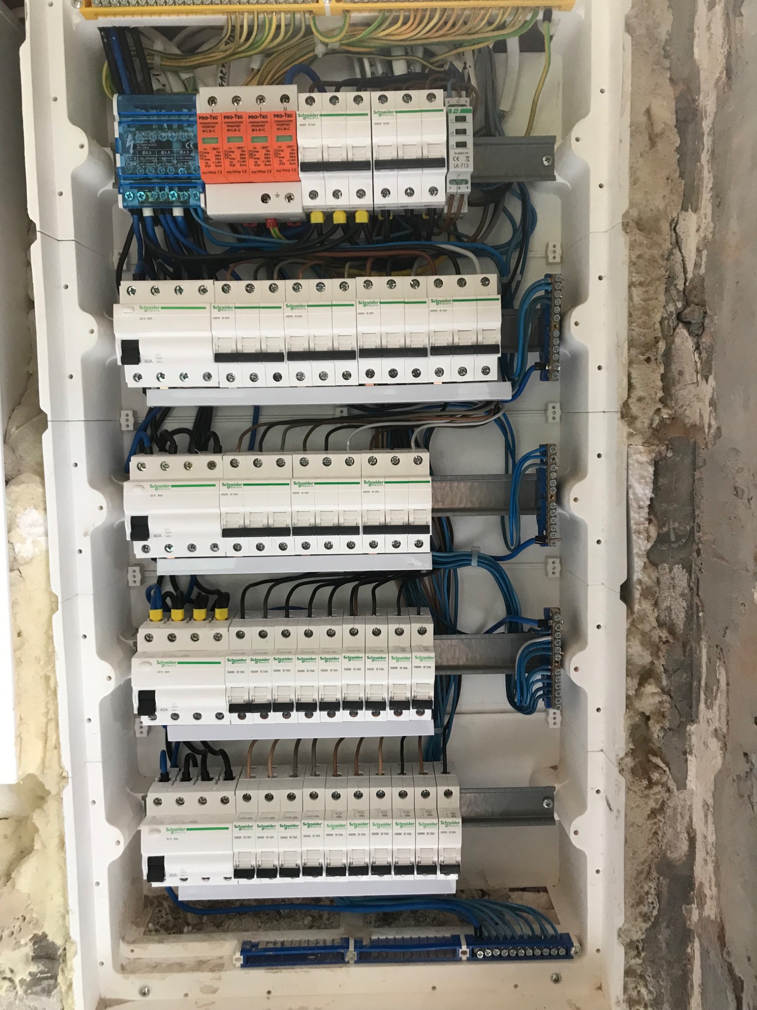 Rozdzielnica elektryczna z zabezpieczeniami przepięciowymi i różnicowoprądowymi w obudowie z białego tworzywa, widoczne przewody w kolorach niebieskim, brązowym, żółto-zielonym, zamontowana...