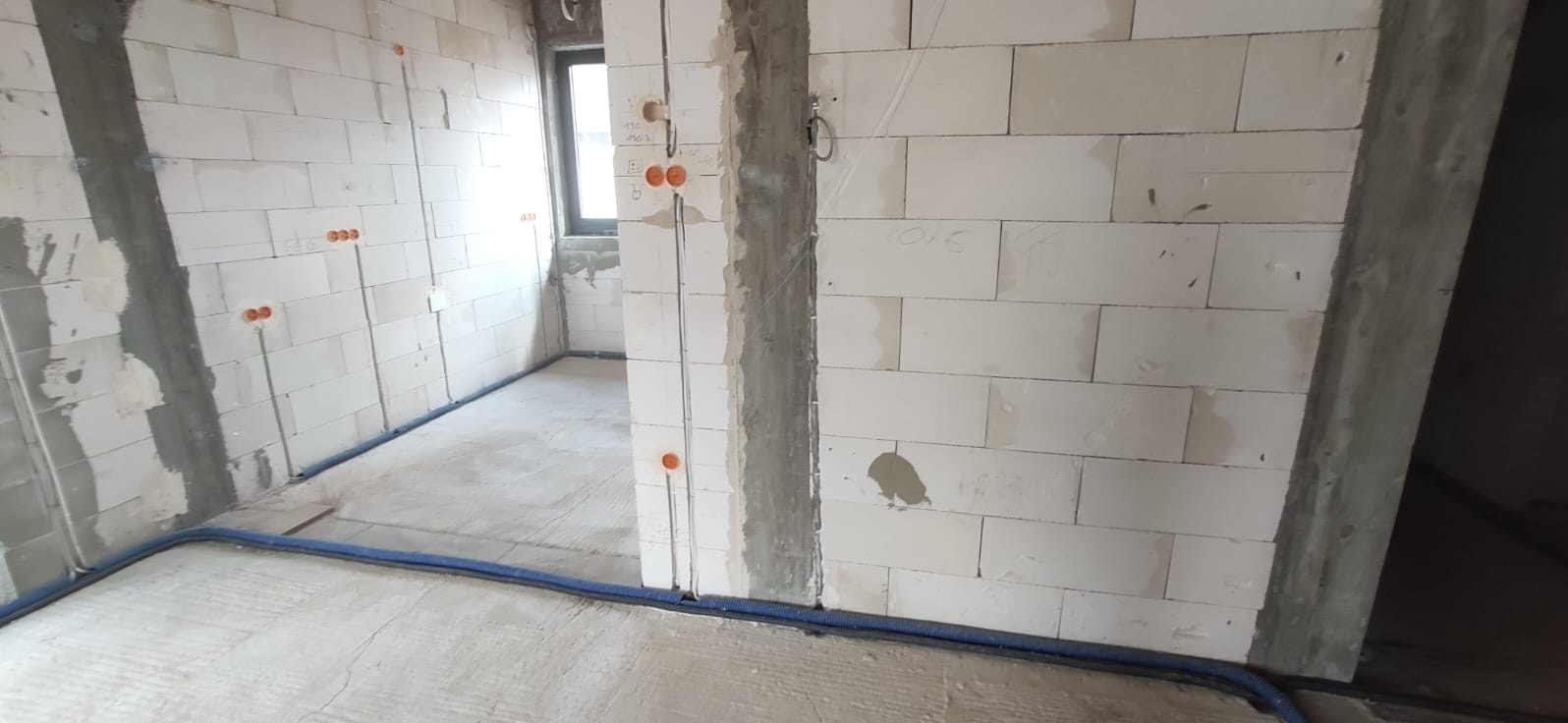 Surowy stan wnętrza z instalacją elektryczną: widoczne kable w peszlach przy podłodze, puszki pod gniazdka w ścianach z betonu komórkowego.