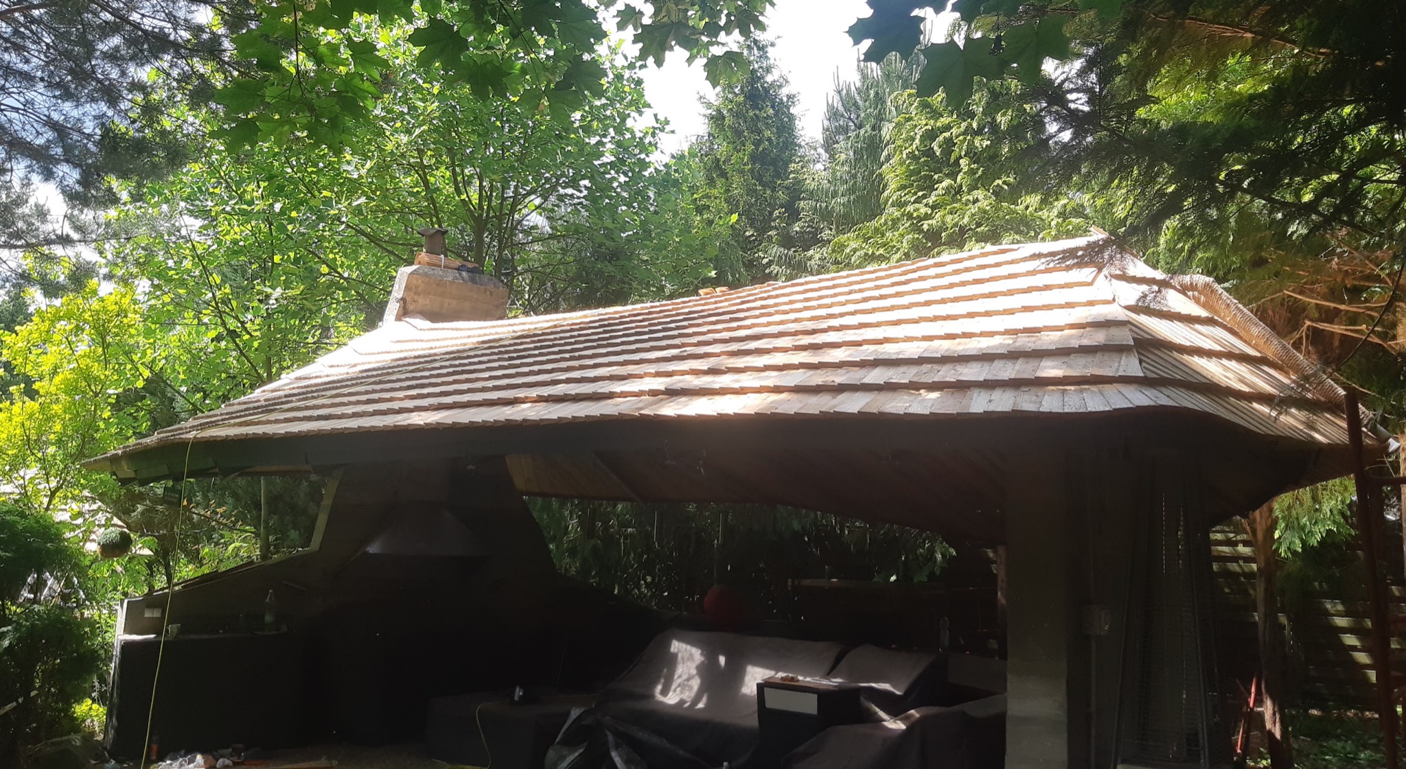 Altana ogrodowa z nowym dachem krytym gontem drewnianym, widok na komin i otaczającą zieleń.