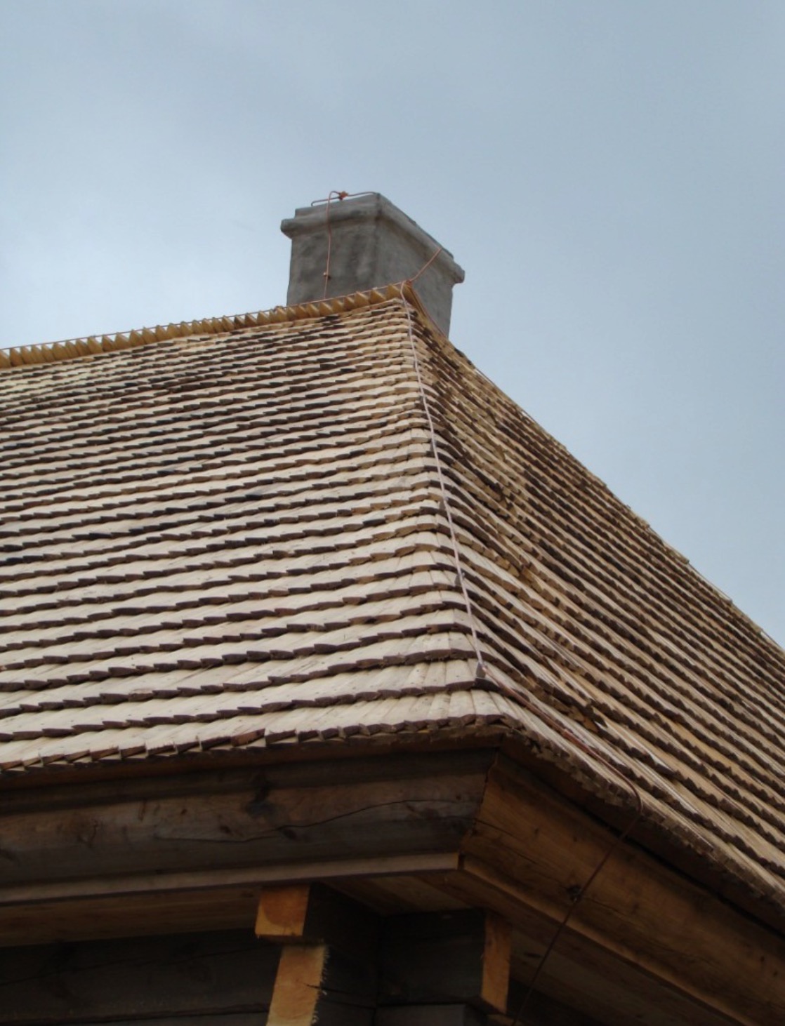 Nowy dach kryty gontem drewnianym, widoczny komin z szarym tynkiem i instalacja odgromowa, drewniana konstrukcja budynku.