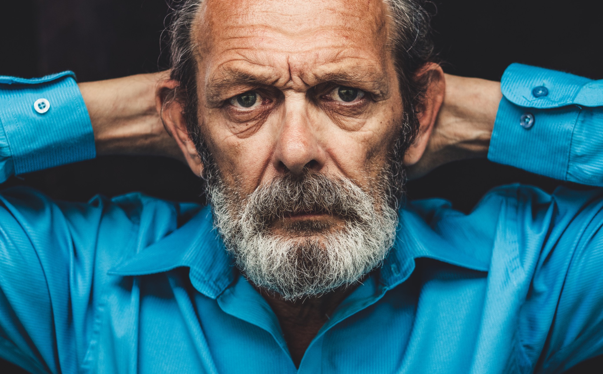 Portret zmęczonego mężczyzny z brodą w błękitnej koszuli, ręce założone za głową, sfotografowany w Ożarowie Mazowieckim.