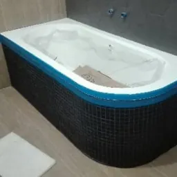 Wanna obudowana mozaiką z niebieskim zabezpieczeniem krawędzi, drabina aluminiowa w rogu, płytki podłogowe w odcieniach beżu, sześciokątne płytki na ścianie.