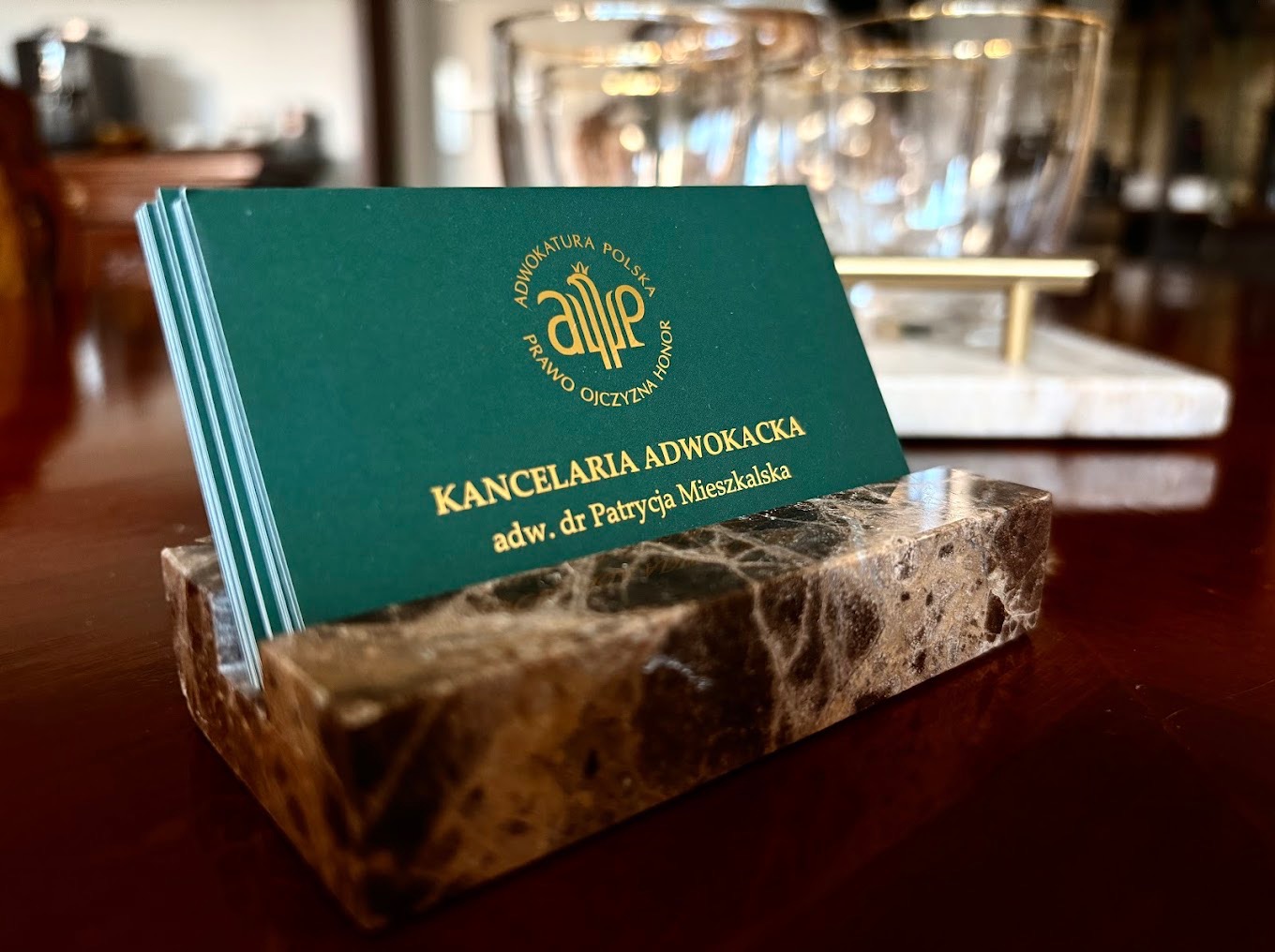 Wizytówki Kancelarii Adwokackiej adw. dr Patrycji Mieszkalskiej w eleganckim, marmurowym podajniku na biurku. Złoty nadruk na zielonym tle.