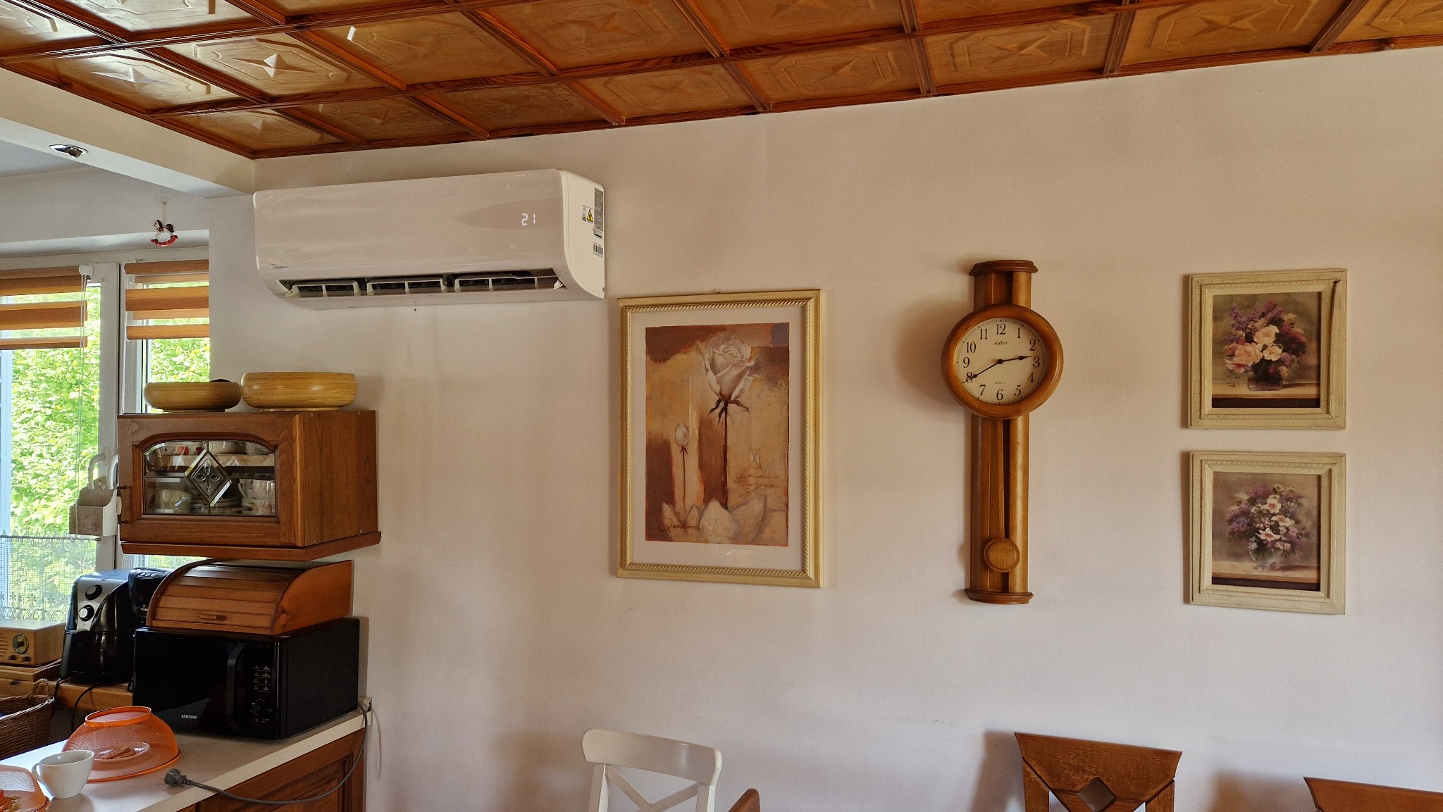 Biała jednostka klimatyzacji Midea zamontowana na ścianie w mieszkaniu we Włoszczowie, nad obrazem z motywem róży i drewnianym zegarem wiszącym.