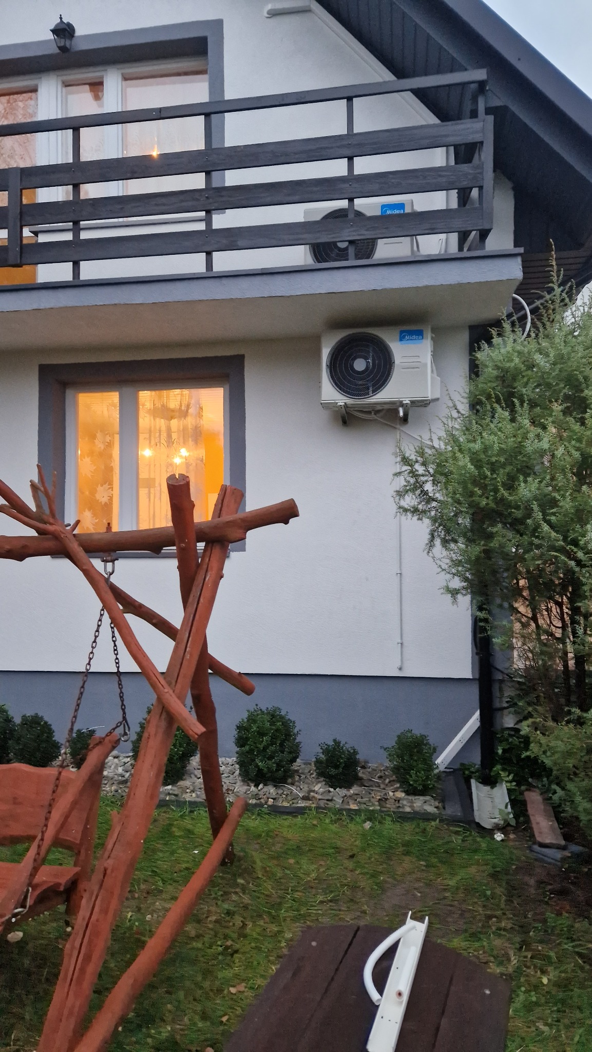Dwa klimatyzatory Midea zamontowane na elewacji domu z drewnianą huśtawką w ogrodzie, widoczne rury odprowadzające skropliny.
