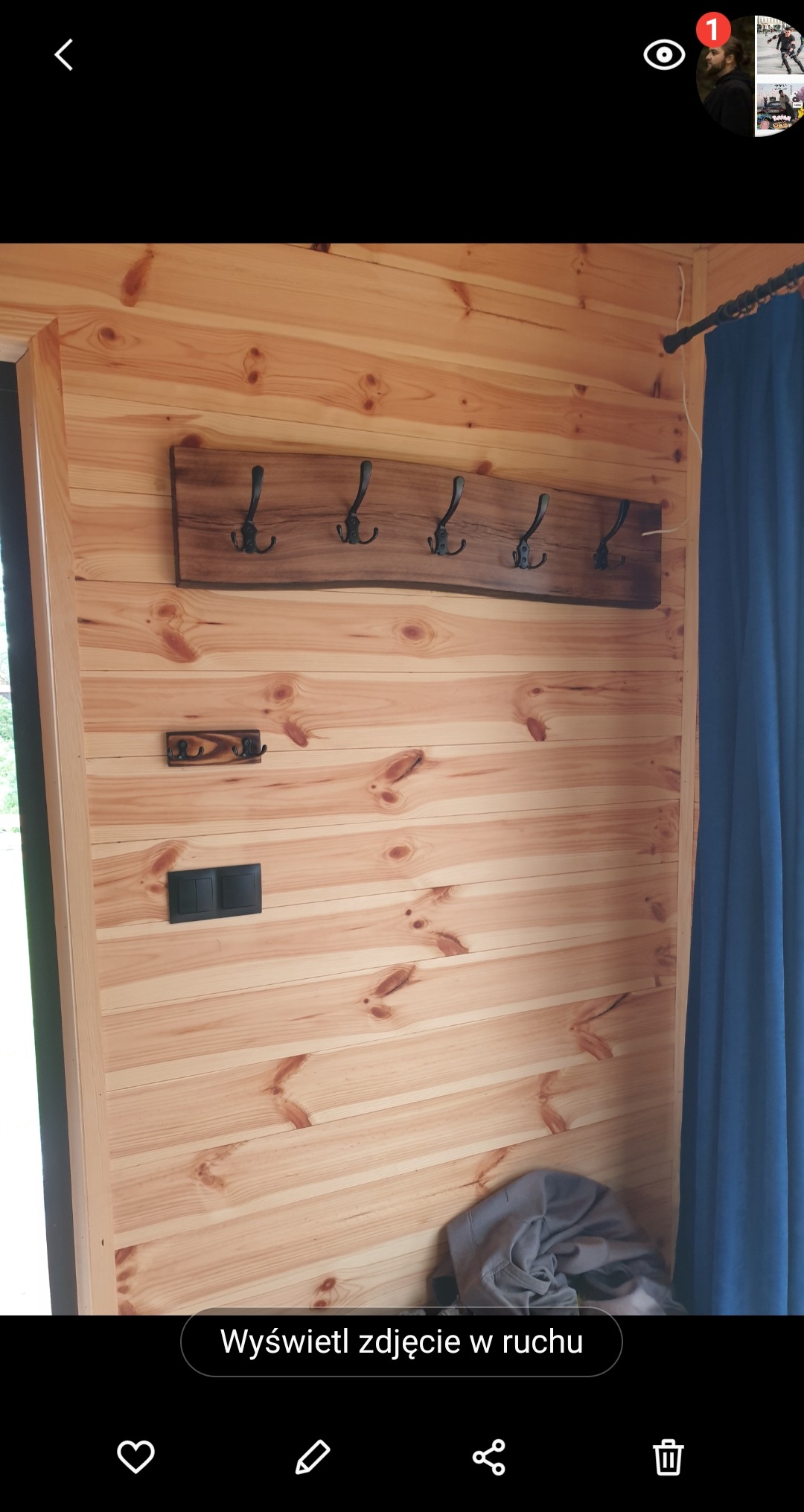 Drewniana ściana z boazerii z zamontowanym rustykalnym wieszakiem na ubrania z ciemnego drewna z metalowymi haczykami, dodatkowy mały wieszak poniżej oraz czarny włącznik światła.