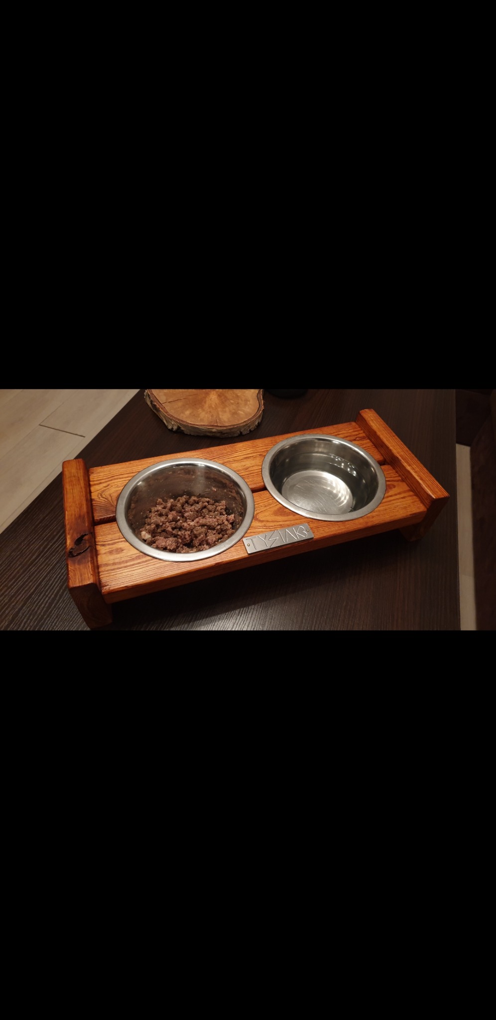 Drewniany stojak na dwie miski dla zwierząt, jedna wypełniona karmą, druga wodą, z wygrawerowanym imieniem 'TYSIĄK'.