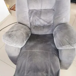 Szary, welurowy fotel typu recliner z widocznymi plamami i śladami użytkowania na siedzisku, oparciu i podłokietnikach, sfotografowany z góry w jasnym wnętrzu.