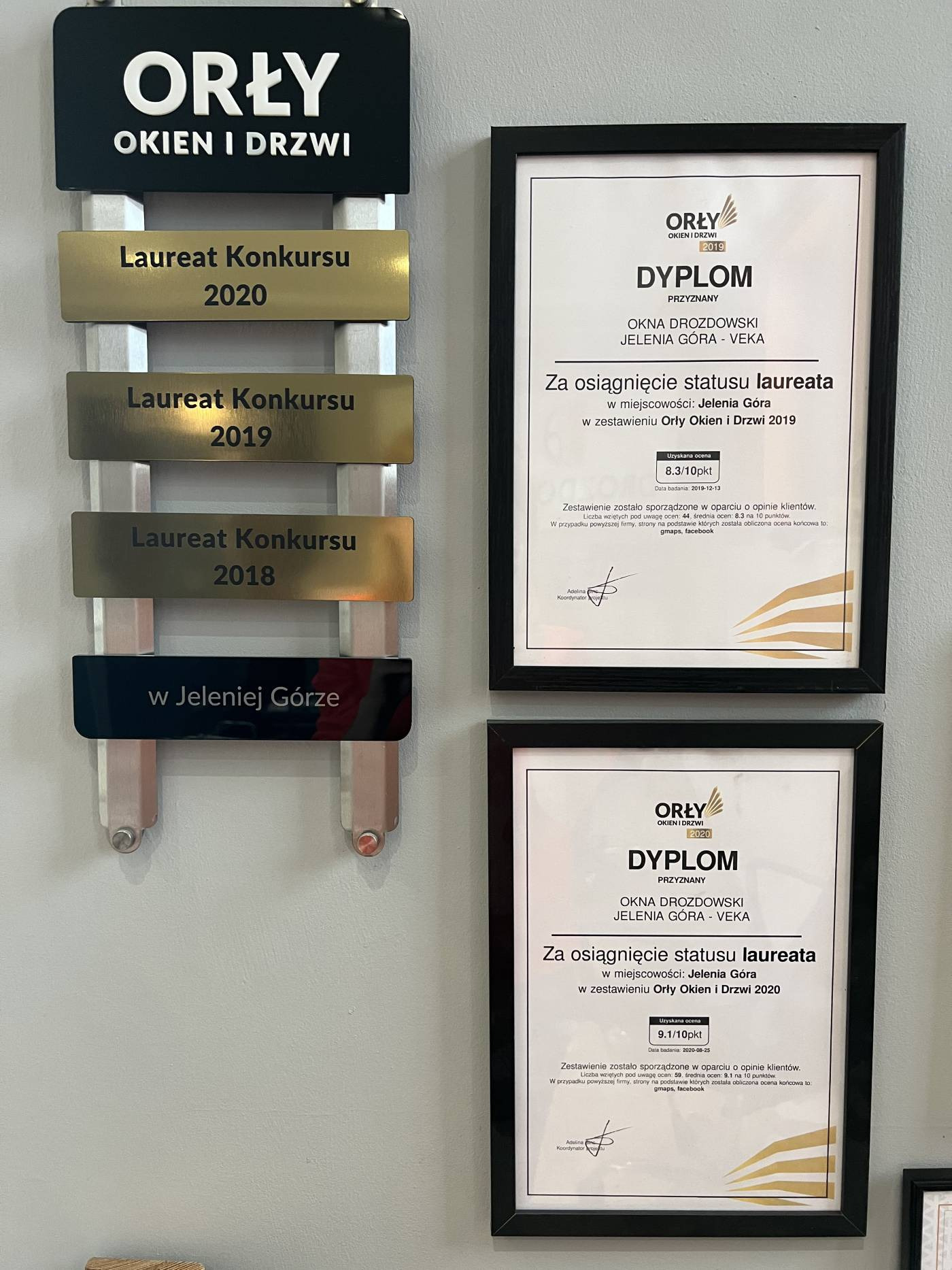 Tablica z logo firmy 'Orły Okien i Drzwi' i informacją o zdobyciu tytułu Laureata Konkursu w latach 2018, 2019 i 2020, obok dyplomy potwierdzające status laureata w latach 2019 i 2020, w czarnych...