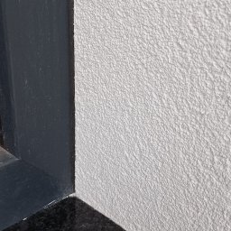 USŁUGI TYNKARSKO-BUDOWLANE - Szara ściana z tynkiem barankiem, ciemna rama okienna i czarny granitowy parapet.