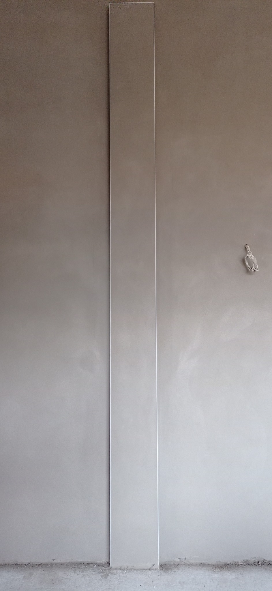 Ściana po nałożeniu szarej gładzi z pionową listwą przypodłogową, widoczne niedoskonałości i wystający kabel elektryczny.