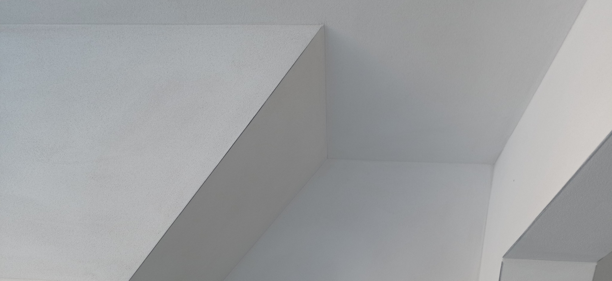 Wnętrze pomalowane na biało z widocznym fragmentem sufitu z załamaniem i ścianą w rogu pomieszczenia.