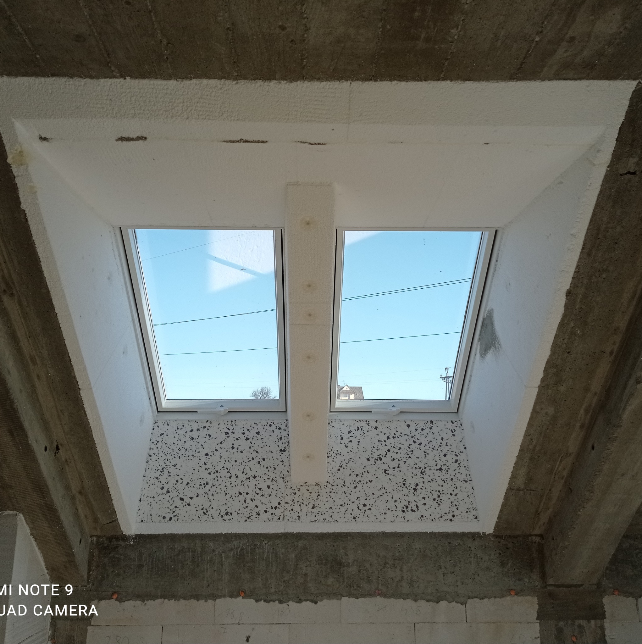 Dwa okna dachowe w trakcie montażu, ocieplone styropianem, widoczne surowe betonowe elementy konstrukcyjne stropu.