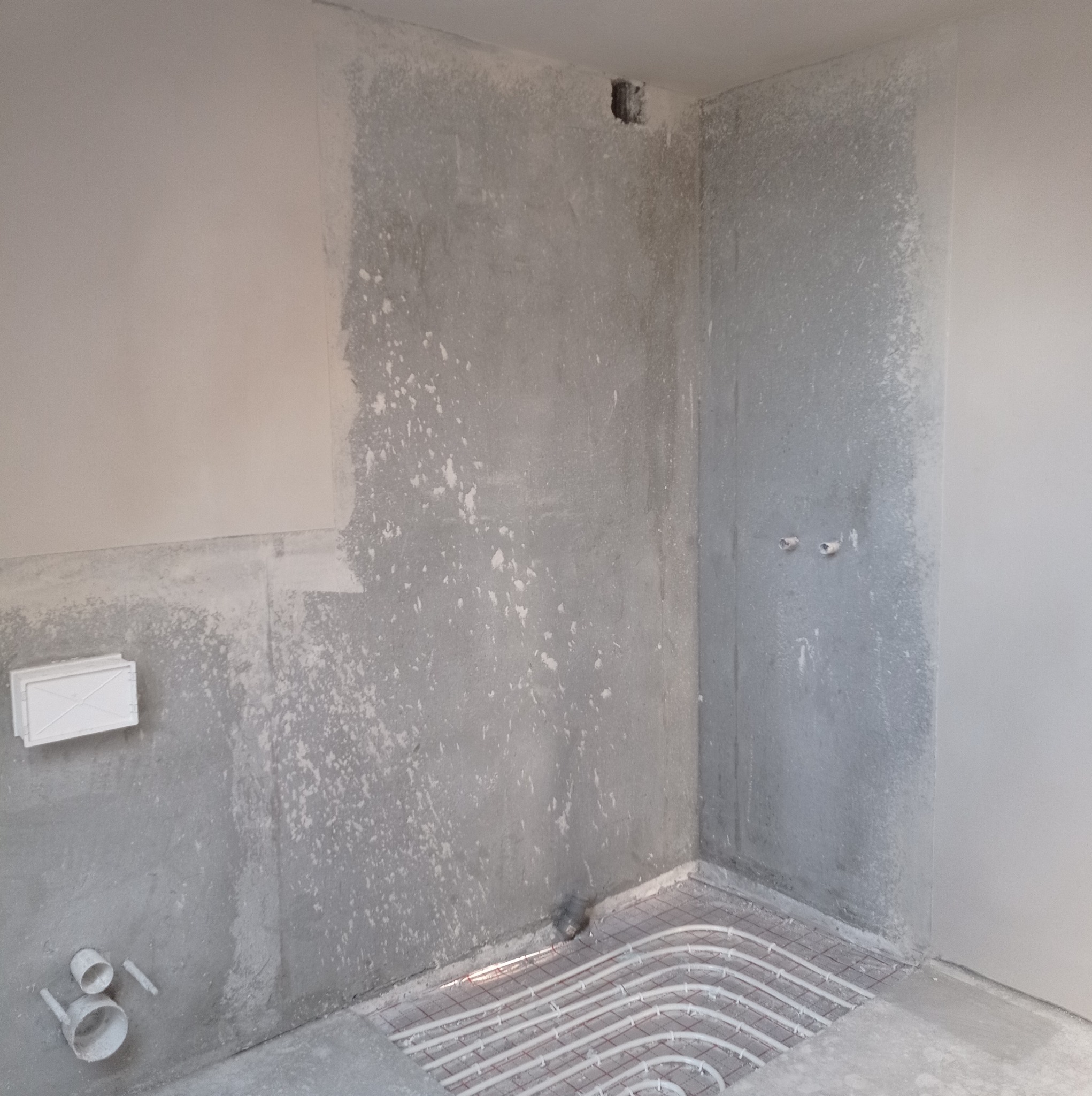 Surowe ściany po szpachlowaniu z widocznymi śladami gładzi, instalacja ogrzewania podłogowego z rurkami w podłodze, przygotowanie do dalszych prac wykończeniowych.