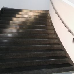 ŁADNY DOM - Ciemne, granitowe schody w budynku biurowym, z jasnymi ścianami i metalową poręczą, widoczne z dołu, z lekkim odblaskiem światła na stopniach.