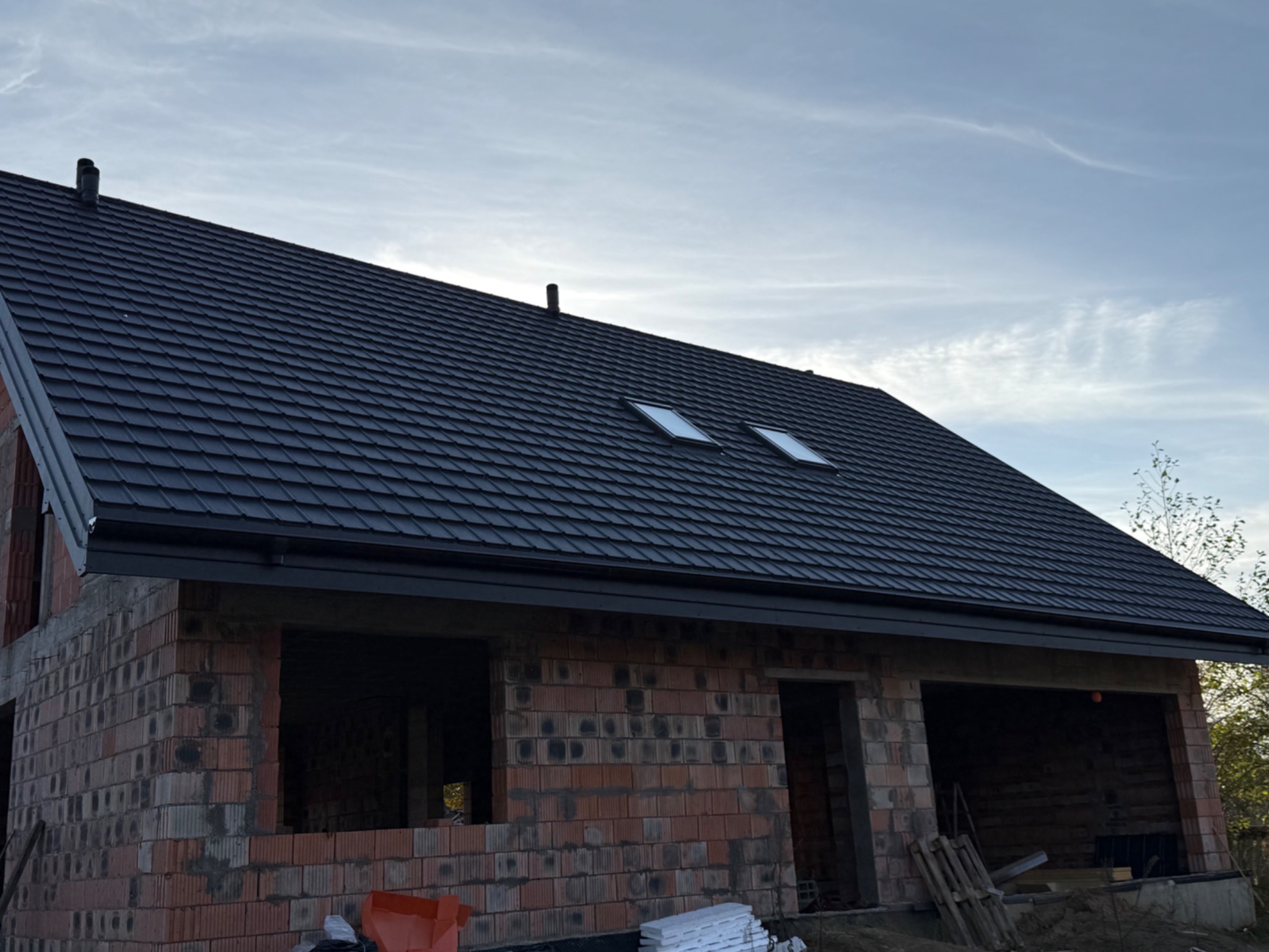 Ciemny dach z dwoma oknami dachowymi na surowym budynku z czerwonej cegły w trakcie budowy, widok z dołu.