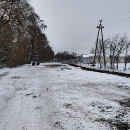 PREMIUMSTAL SEBASTIAN PRZYBYSZ - Zimowy krajobraz z widokiem na nowo postawione ogrodzenie z siatki, częściowo zasypane śniegiem, z widocznym autem dostawczym w tle i słupami energetycznymi