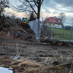 PREMIUMSTAL SEBASTIAN PRZYBYSZ - Nowo postawione, ocynkowane ogrodzenie z siatki, widoczne z perspektywy ziemi, z koparką w tle przygotowującą teren, dom w oddali.