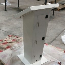 PREMIUMSTAL SEBASTIAN PRZYBYSZ - Biała metalowa szafka zamykana na klucz, z blatem nachylonym pod kątem, stojąca na folii bąbelkowej w hali produkcyjnej, widoczny klucz w zamku i śrubokręt obok.