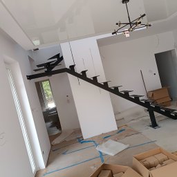PREMIUMSTAL SEBASTIAN PRZYBYSZ - Nowoczesne, czarne schody metalowe bez balustrady, zamontowane w surowym wnętrzu z widocznymi instalacjami i kartonami. Minimalistyczny design, jasne ściany, sufit podwieszany.