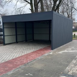 PREMIUMSTAL SEBASTIAN PRZYBYSZ - Nowoczesna, dwustanowiskowa wiata garażowa z szarej blachy trapezowej, na kostce brukowej. Widoczne drzewa w tle. Minimalistyczny design, proste linie.