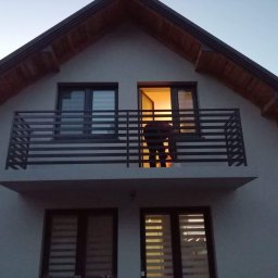 PREMIUMSTAL SEBASTIAN PRZYBYSZ - Nowoczesna, pozioma, metalowa konstrukcja na balkonie domu jednorodzinnego, widok z dołu, w tle sylwetka osoby wewnątrz.