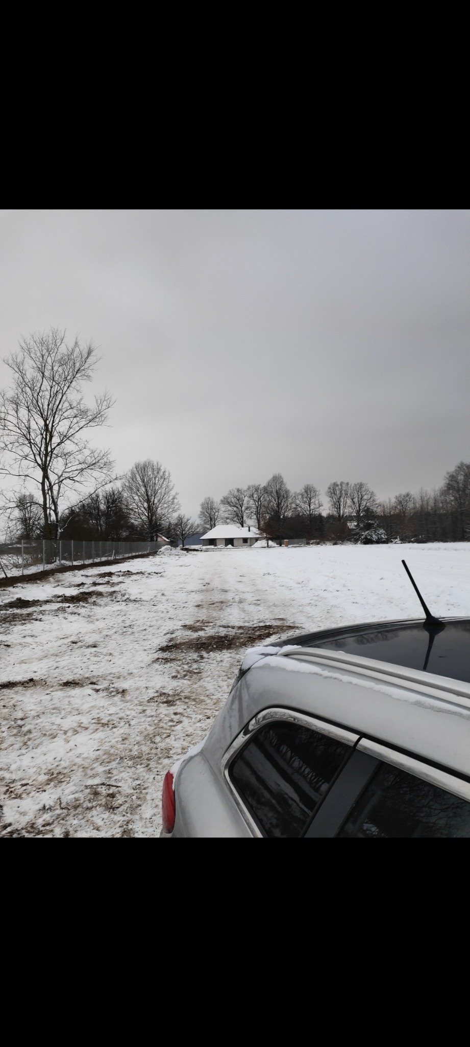 Montaż ogrodzenia panelowego w Tłuszczu zimą, widok zza samochodu na teren z nowym ogrodzeniem i domem w oddali.