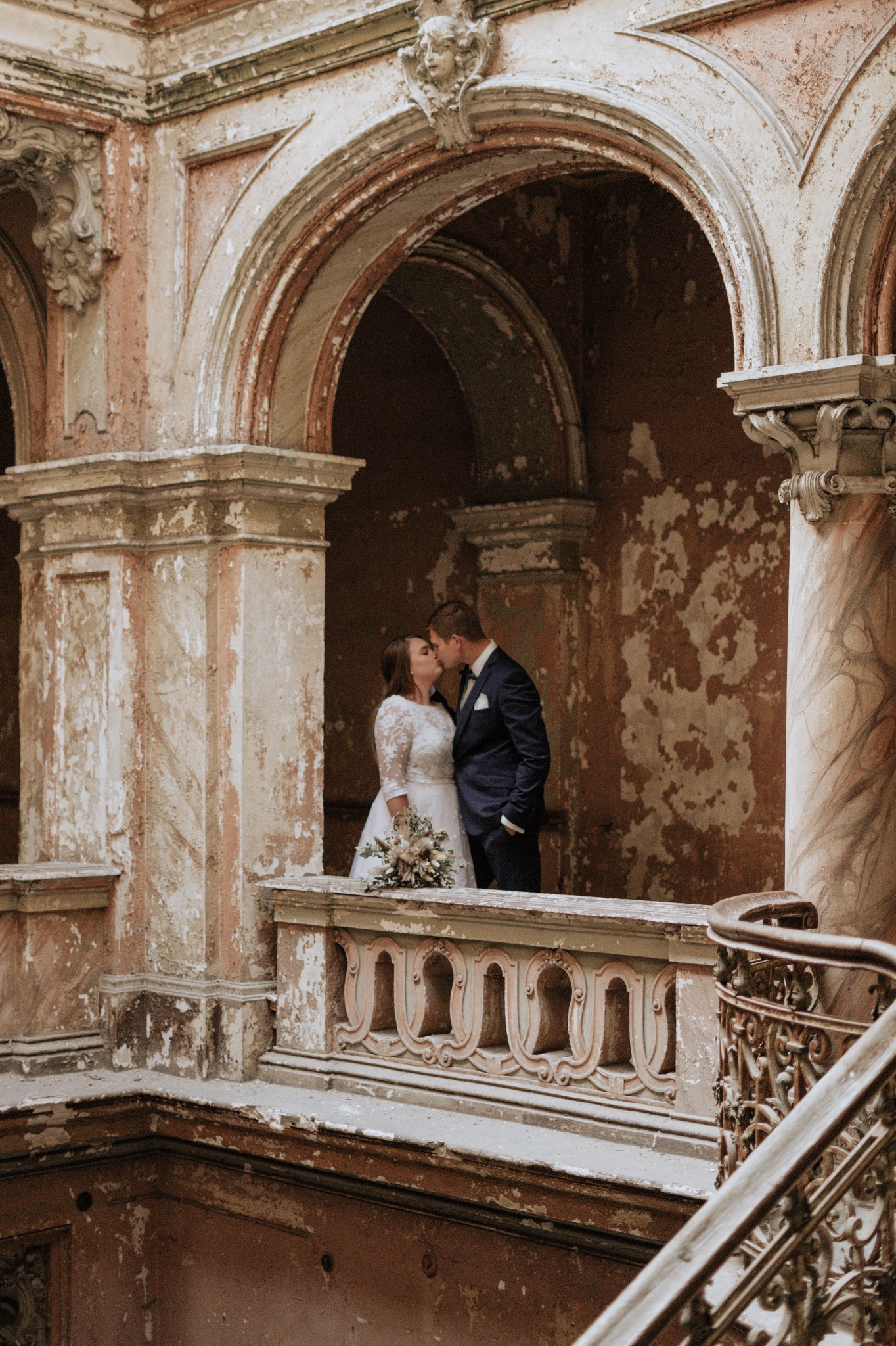 Pocałunek pary młodej na tle zabytkowej architektury z łuszczącą się farbą i marmurowymi kolumnami.