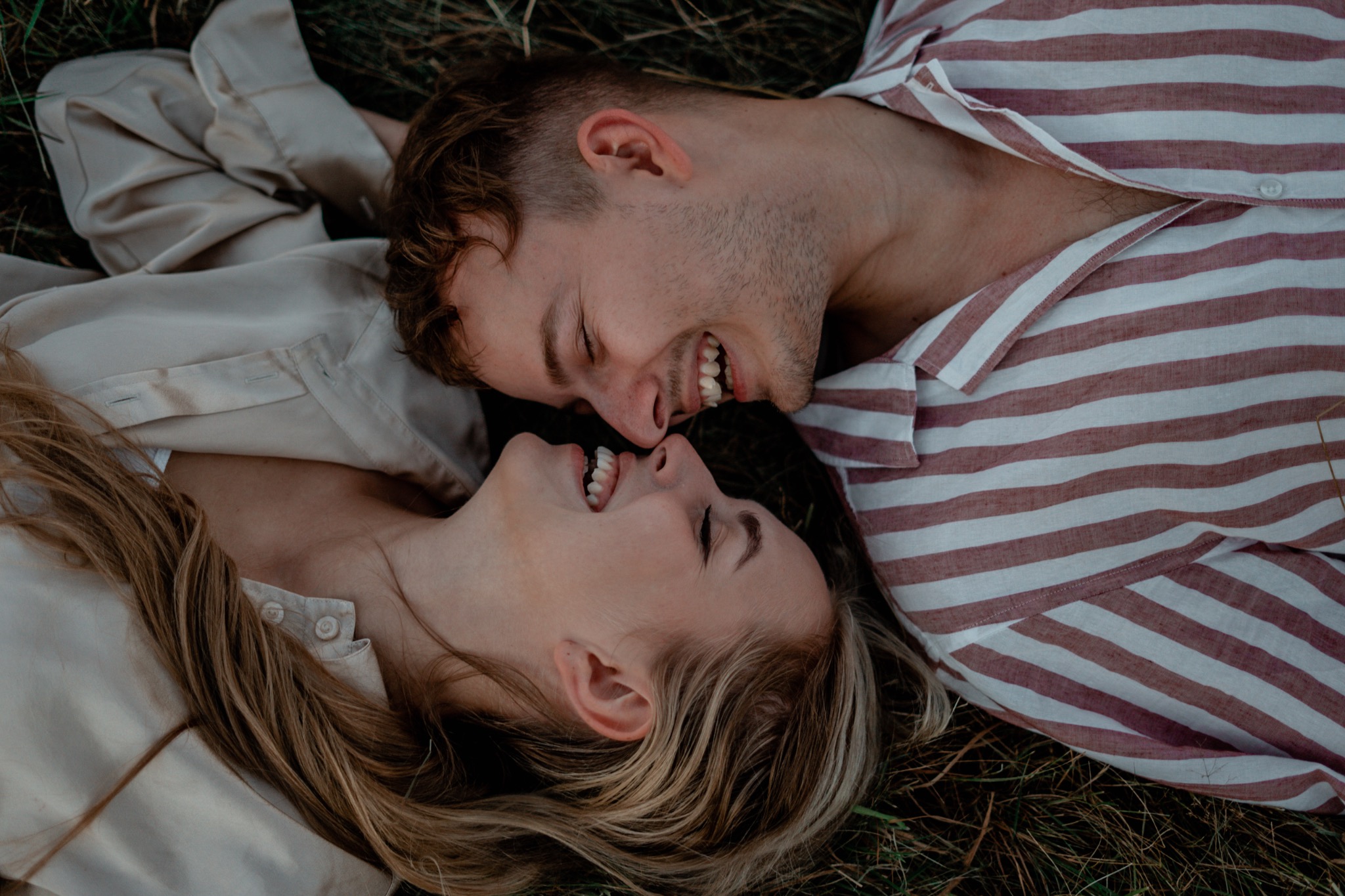 Szczęśliwa para leżąca na trawie, zbliżone twarze, uśmiechy i naturalne światło.