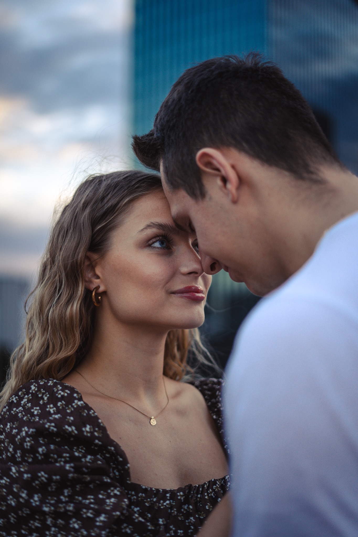 Zakochana para, zbliżenie twarzy, ona patrzy na niego z uśmiechem, w tle nowoczesny budynek.