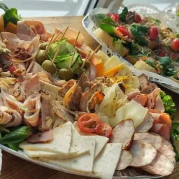 Dekoracyjnie ułożone na paterach wędliny, sery, oliwki na wykałaczkach i bagietki z warzywami, tworzące elegancką kompozycję.