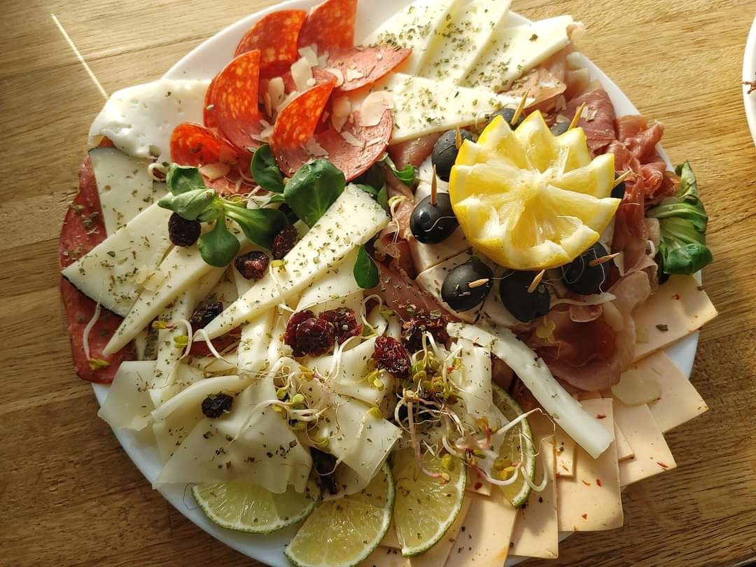 Dekoracyjnie ułożona na białym talerzu kompozycja wędlin, serów, oliwek, plasterków cytryny i limonki, suszonej żurawiny oraz kiełków, zwieńczona rzeźbionym cytrynowym kwiatem.