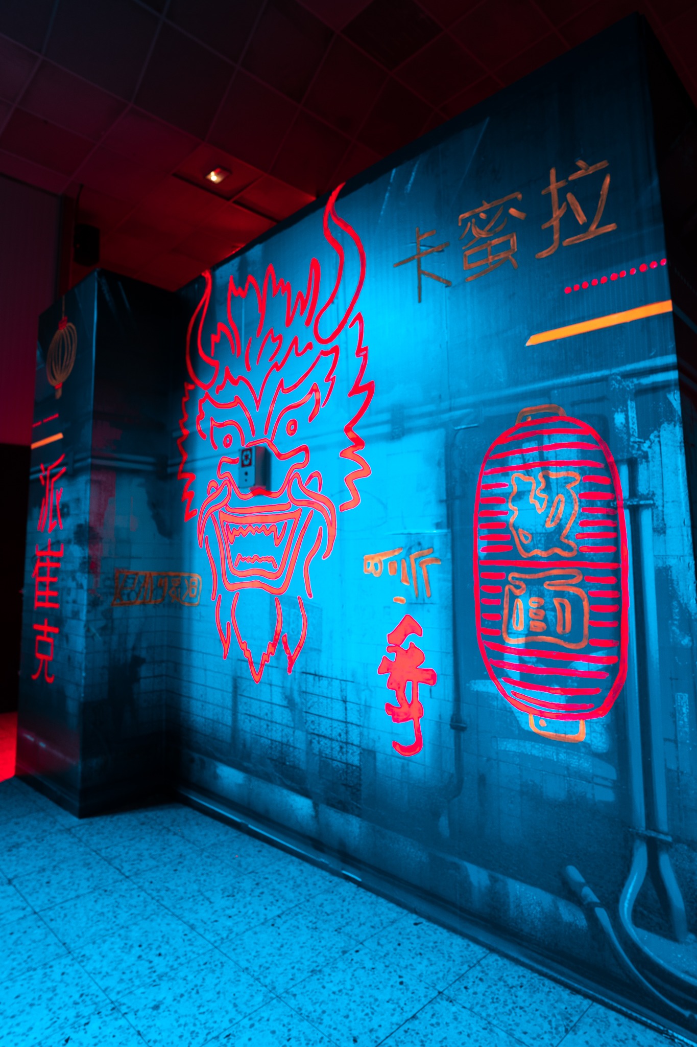 Scena z neonowymi azjatyckimi motywami, smok i lampiony na tle ściany w Bydgoszczy, oświetlona czerwonym i niebieskim światłem.