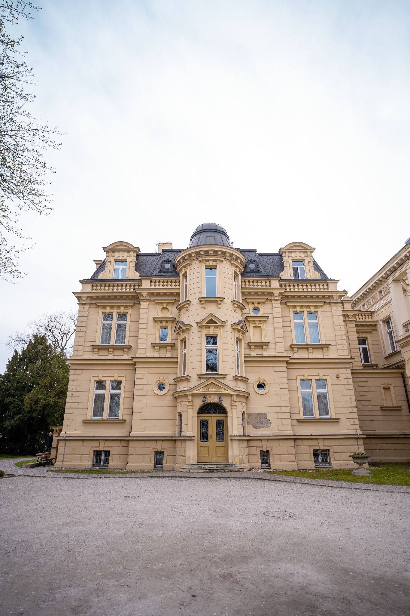 Elewacja secesyjnej kamienicy z wieżyczką i zdobieniami, widok z dołu na tle pochmurnego nieba.