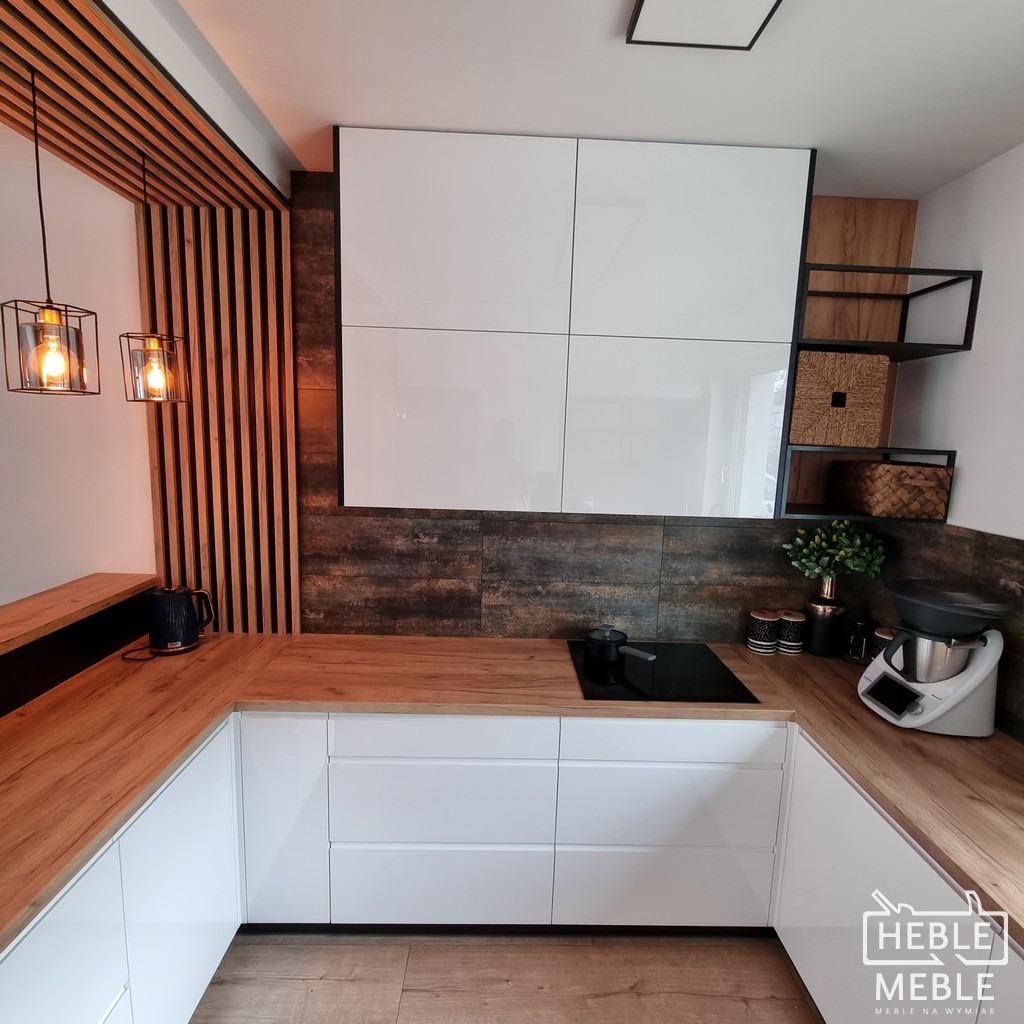 Nowoczesna kuchnia na wymiar z białymi szafkami, drewnianym blatem i dekoracyjną ścianką z drewnianych listew oraz industrialnymi lampami wiszącymi.